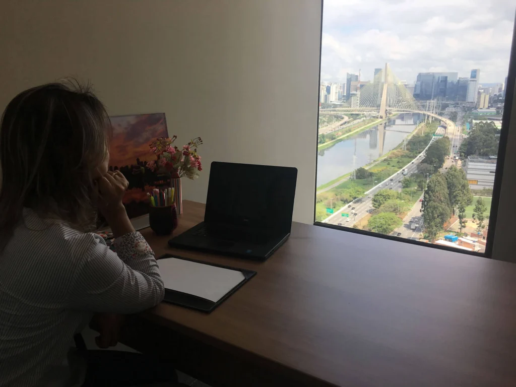 Rejane sentada, em frente ao notebook, com a vistas de São Paulo a sua frente