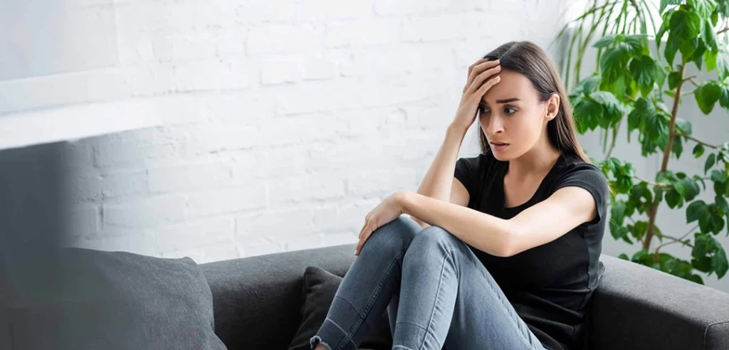 uma jovem mulher, com expressão aflita, sentada com a mão na cabeça